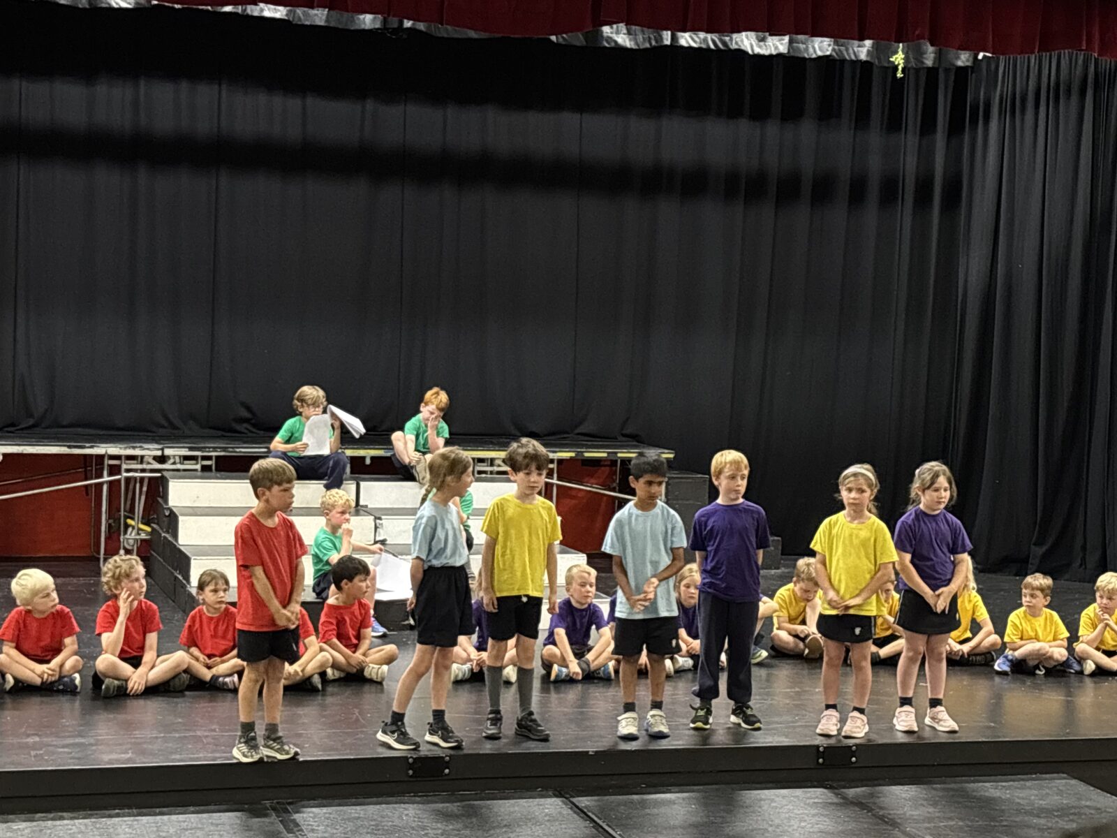 Children in colourful clothing performing on school theatre stage