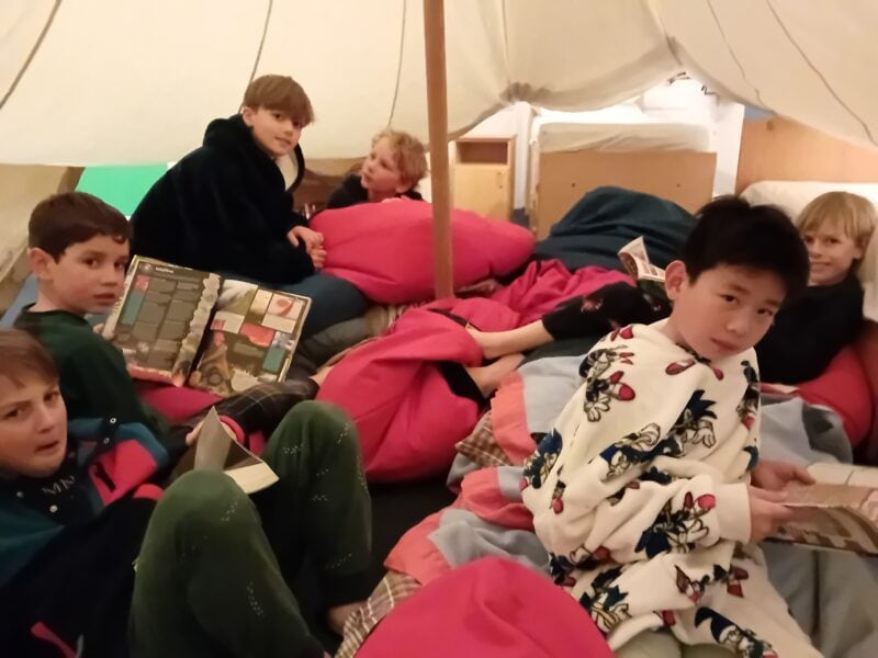 Group of children in a cosy canvas tent reading books on bean bags