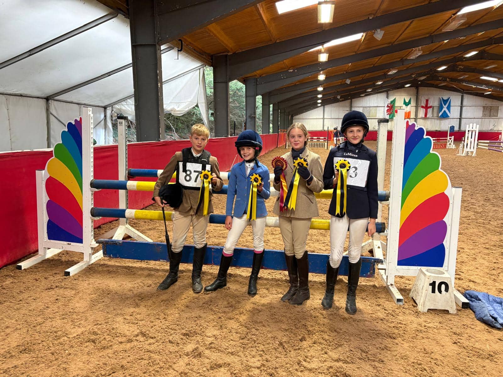 Four young horse riders proudly holding their winners' rosettes