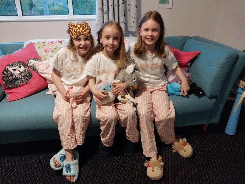 Three girls smiling sat on sofa together
