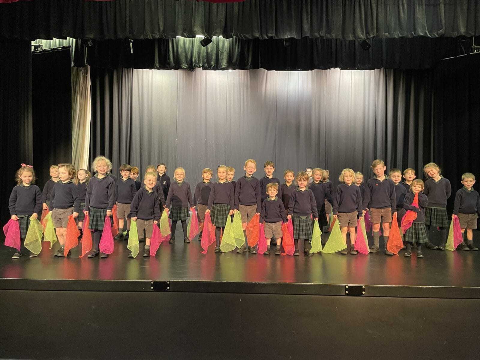 Young children performing on stage with brightly coloured scarves