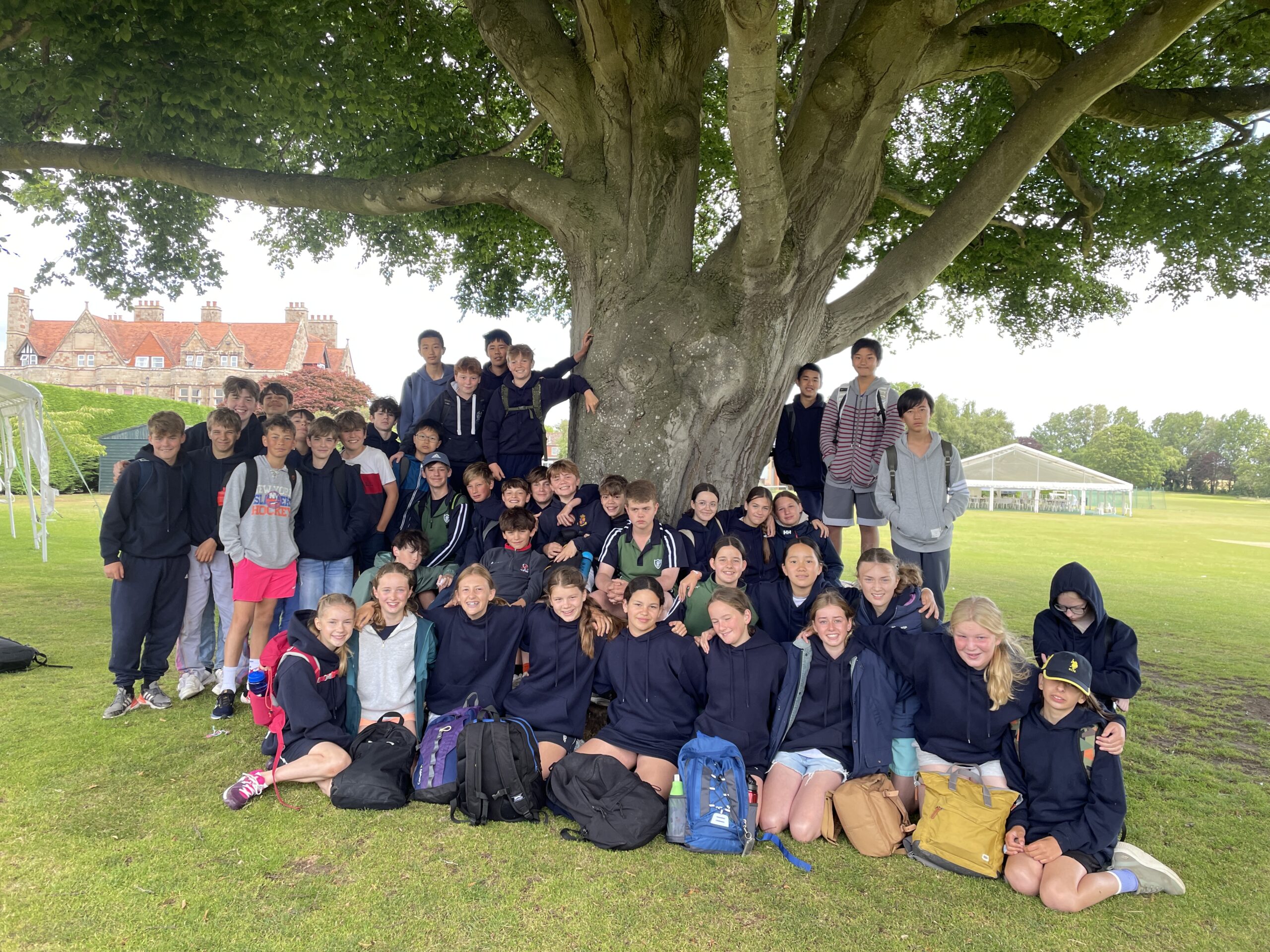 Group of children with rucksacks standing beneath a beautiful tree