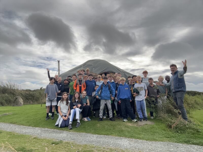 Large group of pupils and staff standing outside a large tent in windy weather