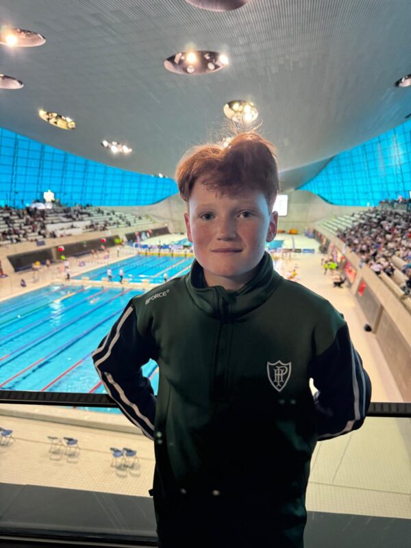 A boy standing in front of the Olympic swimming pool in London.