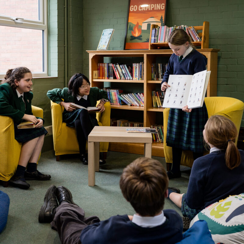 Girl in school uniform showing pages of a book to other children