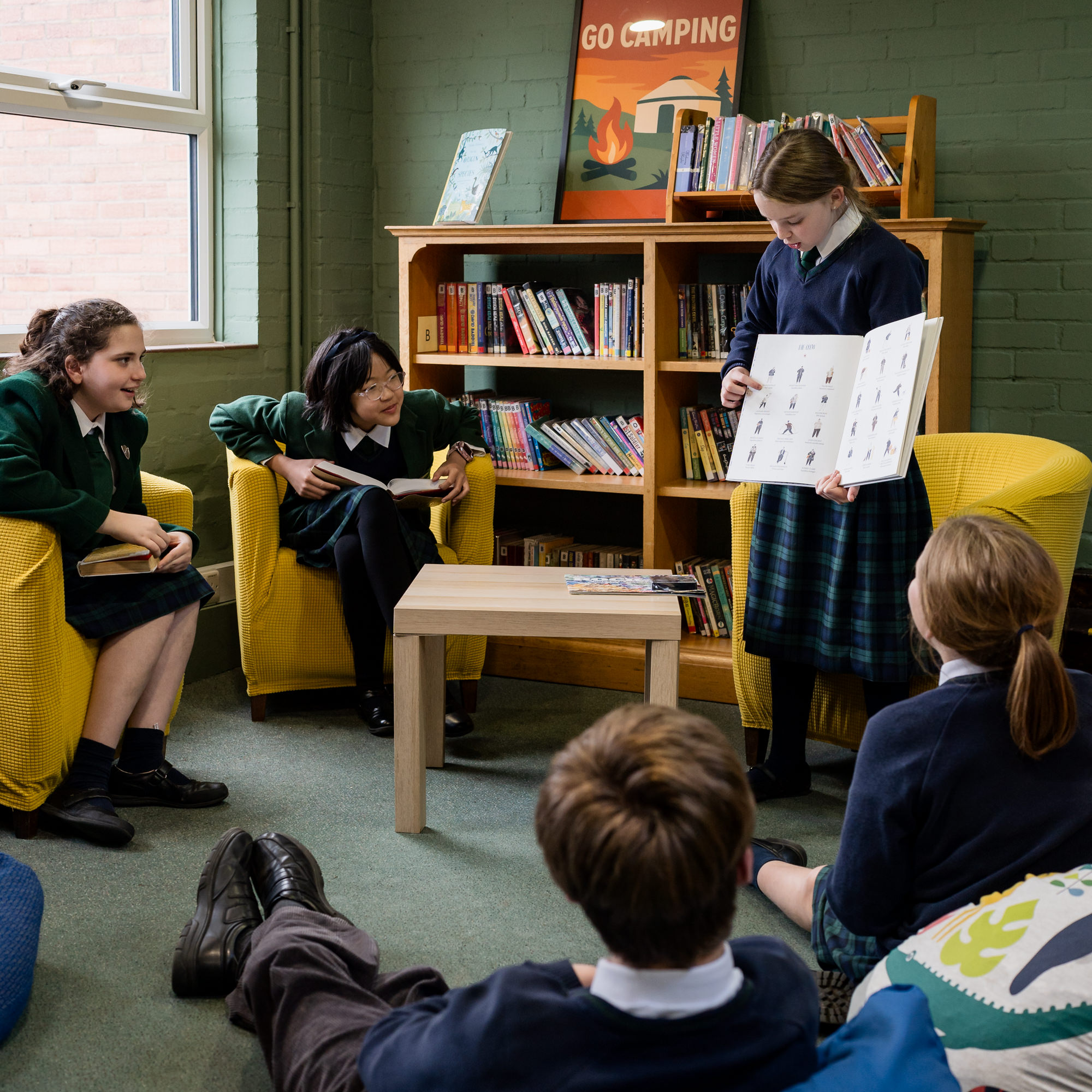 Girl in school uniform showing pages of a book to other children
