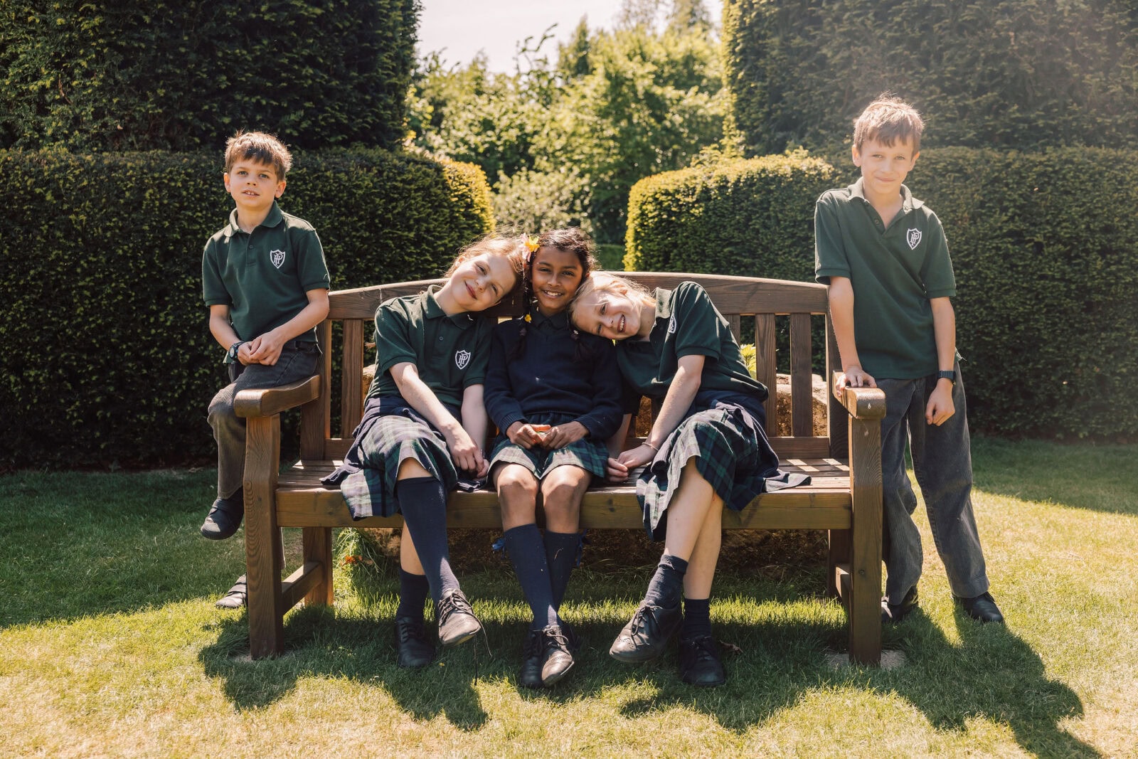Three happy girls and two boys sat on a bench in a school garden