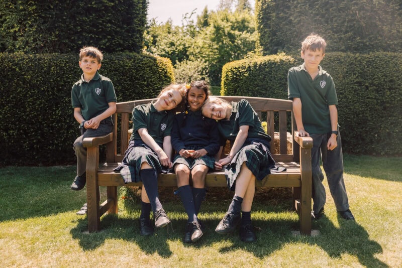 Three happy girls and two boys sat on a bench in a school garden
