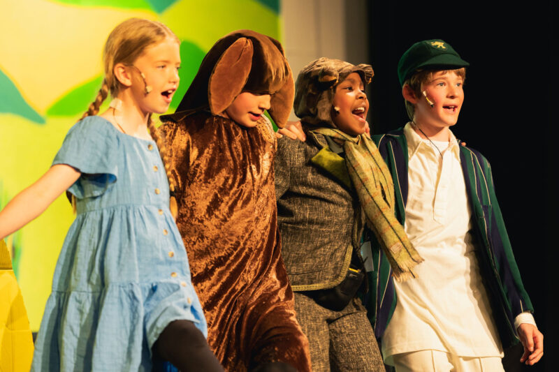 Four children on stage smiling and performing